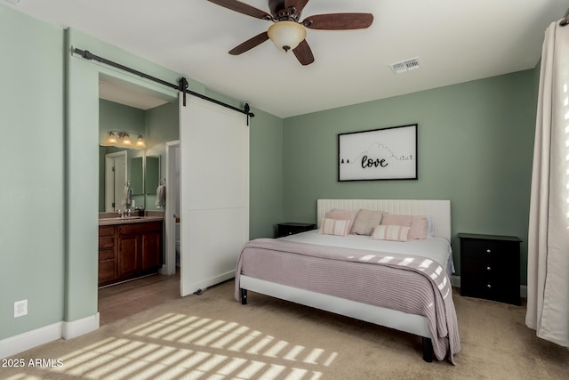 carpeted bedroom with ensuite bathroom, a barn door, and ceiling fan