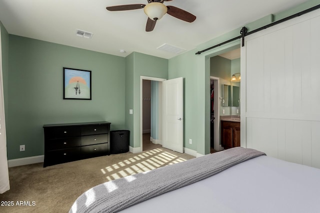 carpeted bedroom with ceiling fan, a barn door, and ensuite bath