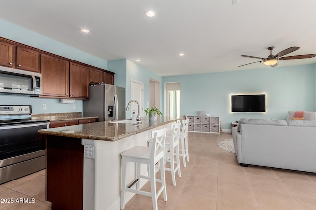 kitchen featuring an island with sink, stainless steel appliances, dark stone countertops, a breakfast bar, and sink