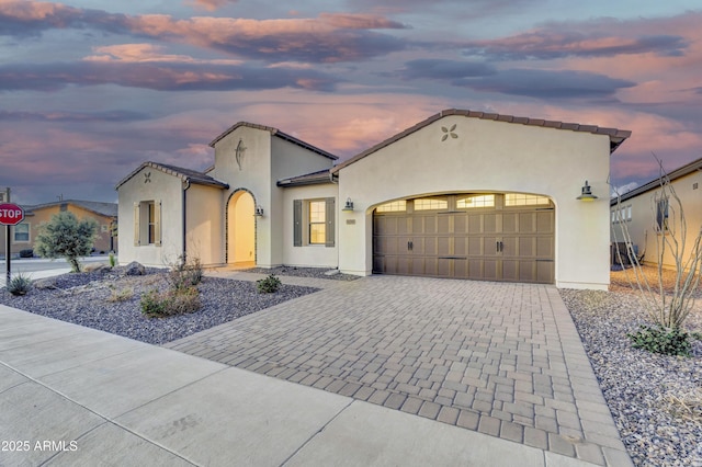 mediterranean / spanish house featuring a garage, a tiled roof, decorative driveway, and stucco siding