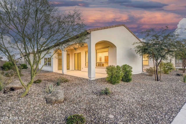 back of house at dusk featuring a patio and stucco siding