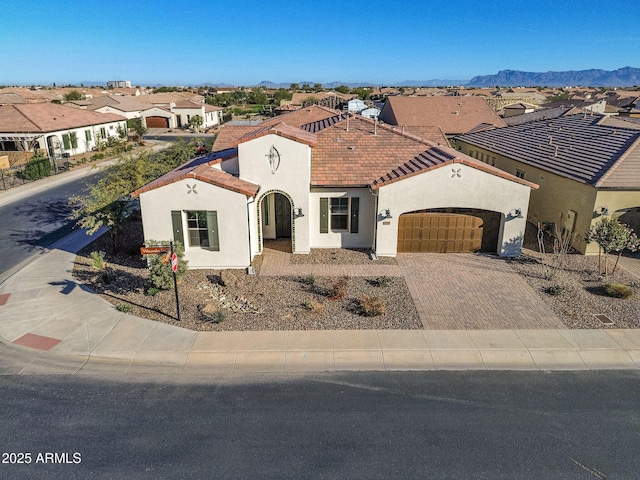 mediterranean / spanish house featuring a tile roof, a residential view, an attached garage, decorative driveway, and stucco siding