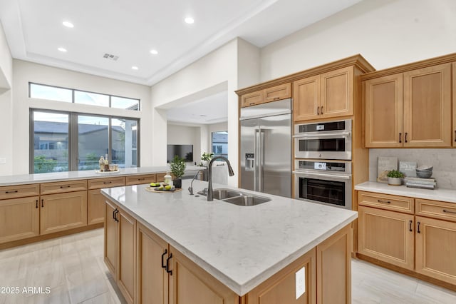 kitchen with appliances with stainless steel finishes, a sink, light stone counters, and an island with sink