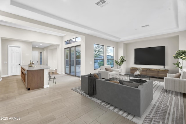 living room with a tray ceiling, french doors, visible vents, light wood-style flooring, and baseboards