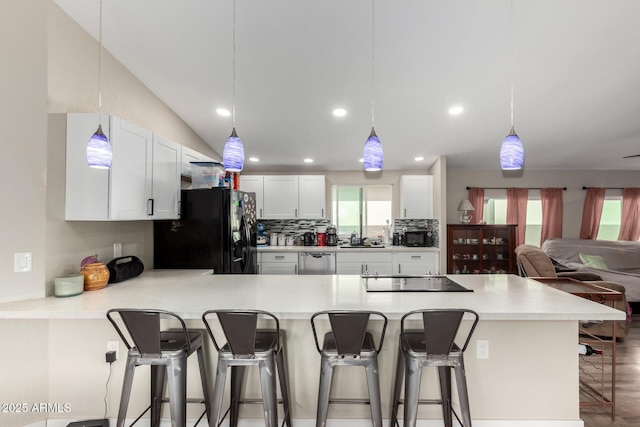 kitchen with black appliances, tasteful backsplash, a peninsula, light countertops, and vaulted ceiling