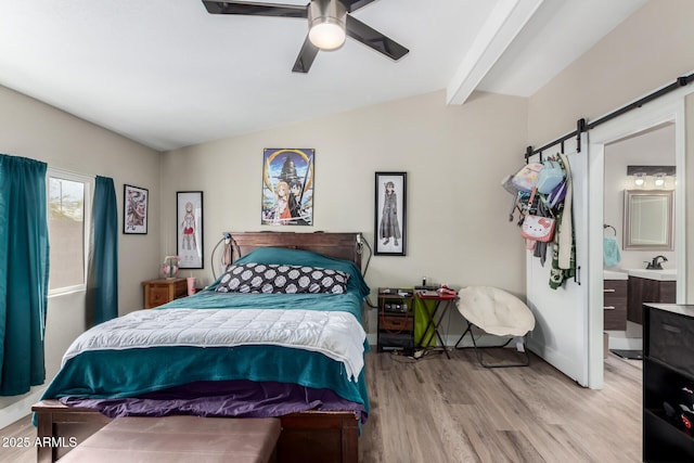 bedroom featuring a barn door, lofted ceiling with beams, light wood finished floors, and a sink