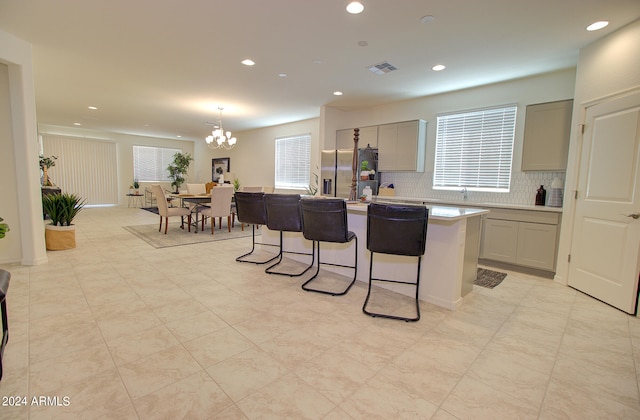 kitchen with gray cabinets, decorative light fixtures, decorative backsplash, stainless steel fridge with ice dispenser, and an island with sink