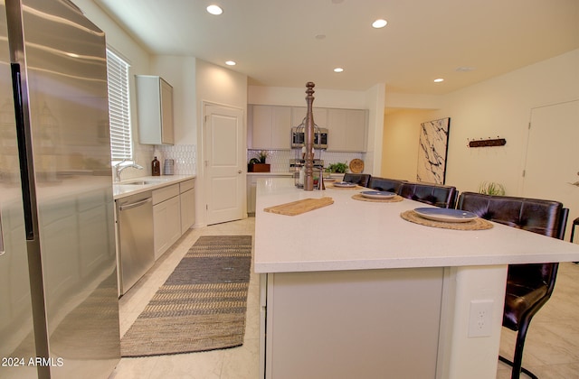 kitchen with gray cabinets, light tile patterned flooring, stainless steel appliances, decorative backsplash, and a center island