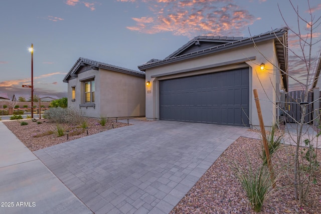 ranch-style home featuring a garage, decorative driveway, a tiled roof, and stucco siding