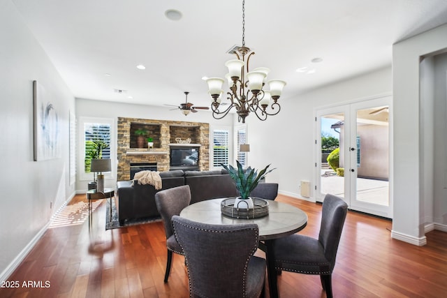 dining room with dark hardwood / wood-style flooring, a wealth of natural light, ceiling fan with notable chandelier, and a fireplace