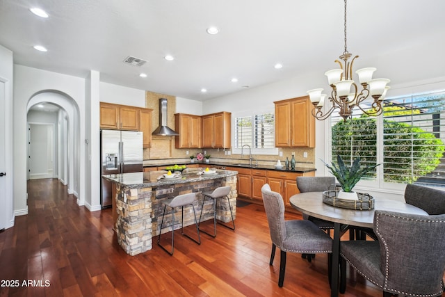 kitchen featuring a kitchen island, dark wood-type flooring, wall chimney range hood, and stainless steel refrigerator with ice dispenser