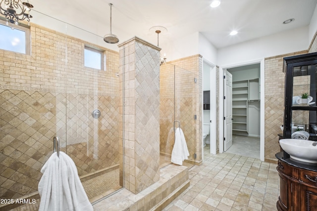 bathroom with vanity, tiled shower, toilet, and tile walls