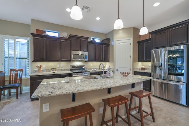 kitchen featuring sink, stainless steel appliances, hanging light fixtures, and an island with sink