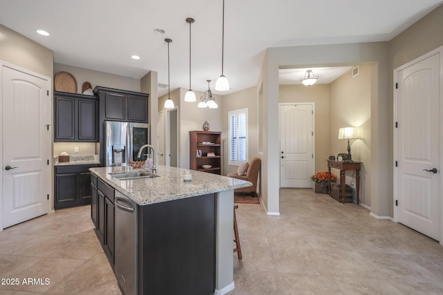 kitchen featuring light stone countertops, sink, stainless steel fridge, pendant lighting, and a center island with sink