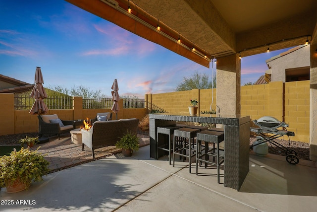 patio terrace at dusk featuring outdoor lounge area, an outdoor bar, and grilling area