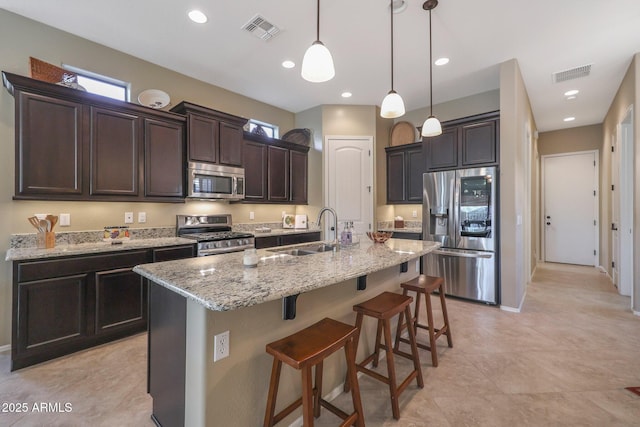 kitchen featuring a center island with sink, sink, decorative light fixtures, dark brown cabinets, and stainless steel appliances