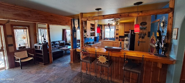 kitchen with butcher block counters, hanging light fixtures, black fridge, kitchen peninsula, and a kitchen bar