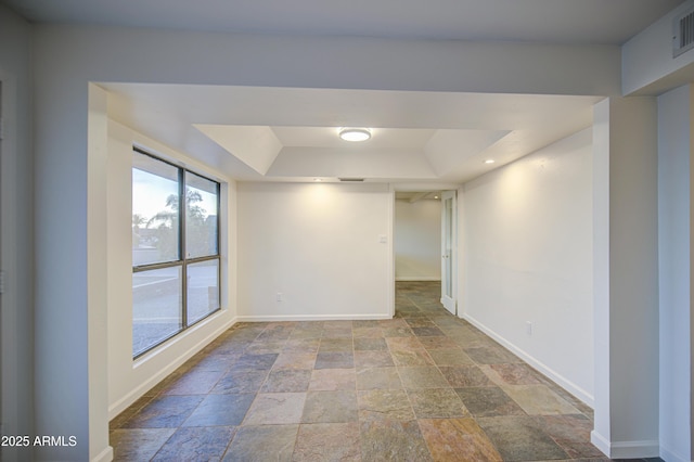 unfurnished room featuring stone tile flooring, a tray ceiling, and baseboards