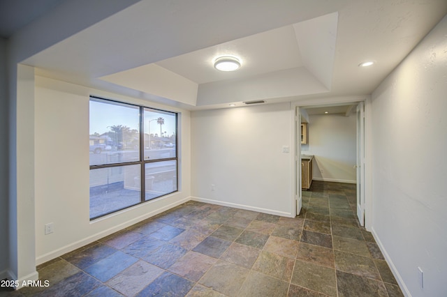 spare room featuring baseboards, visible vents, stone tile flooring, and a tray ceiling