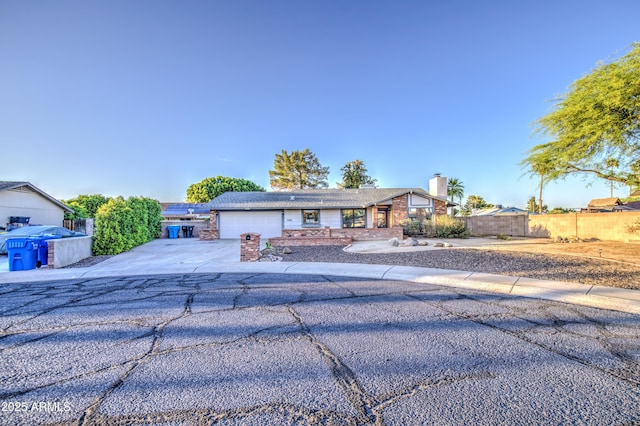 ranch-style house featuring a chimney, fence, concrete driveway, and an attached garage