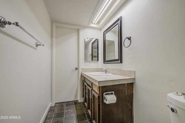 bathroom with toilet, stone finish floor, vanity, and baseboards