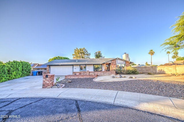 ranch-style home with driveway, a chimney, an attached garage, fence, and brick siding