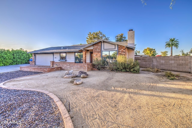 mid-century modern home with fence, a chimney, an attached garage, and brick siding