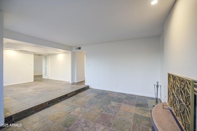 unfurnished room featuring stone tile floors, baseboards, a fireplace with raised hearth, and recessed lighting