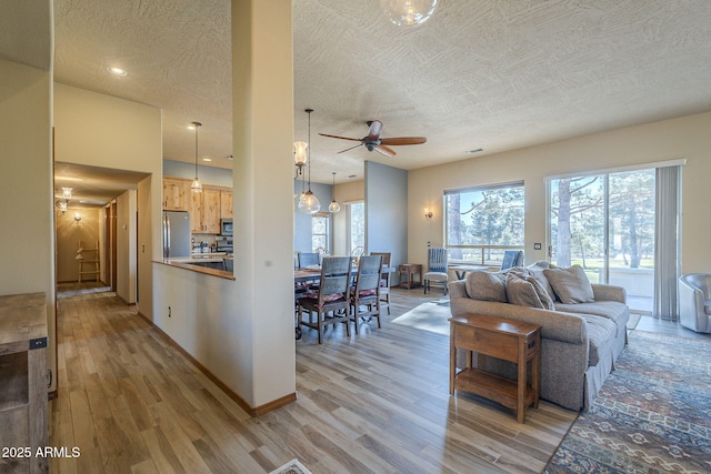 living room featuring light wood-type flooring, ceiling fan, and a textured ceiling