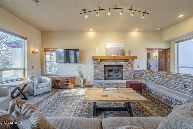 living room featuring rail lighting, wood-type flooring, and a stone fireplace