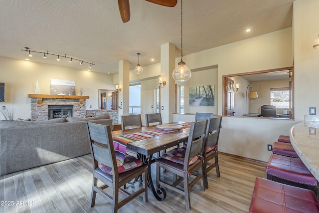 dining room featuring a textured ceiling, ceiling fan, light hardwood / wood-style floors, and a stone fireplace