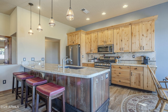 kitchen with light stone countertops, light hardwood / wood-style floors, decorative backsplash, appliances with stainless steel finishes, and sink