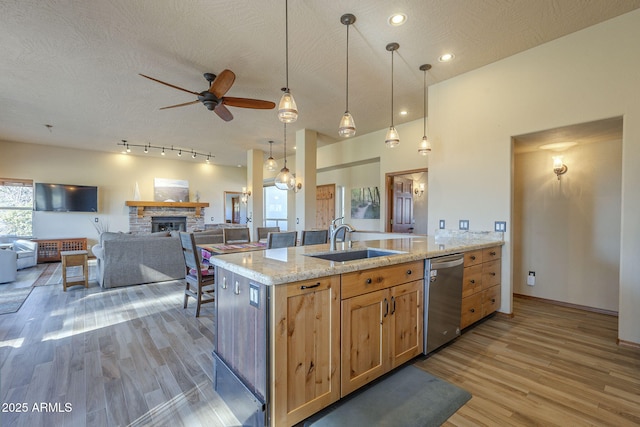 kitchen featuring dishwasher, a stone fireplace, ceiling fan, sink, and decorative light fixtures