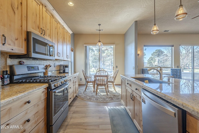 kitchen with appliances with stainless steel finishes, hanging light fixtures, sink, and light brown cabinets