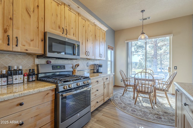 kitchen with light stone counters, hanging light fixtures, stainless steel appliances, light brown cabinetry, and decorative backsplash