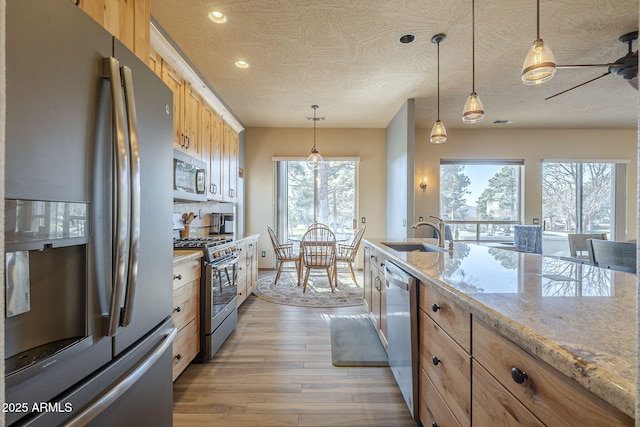 kitchen featuring sink, light stone countertops, pendant lighting, and appliances with stainless steel finishes