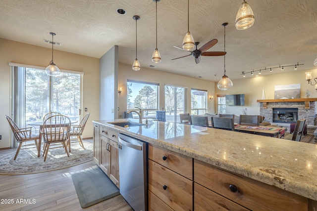 kitchen with light stone counters, dishwasher, pendant lighting, a fireplace, and sink