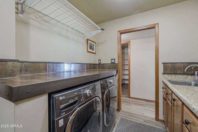 laundry room with sink, washer and dryer, and light hardwood / wood-style floors