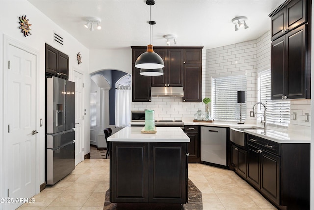 kitchen with a kitchen island, appliances with stainless steel finishes, hanging light fixtures, light countertops, and under cabinet range hood