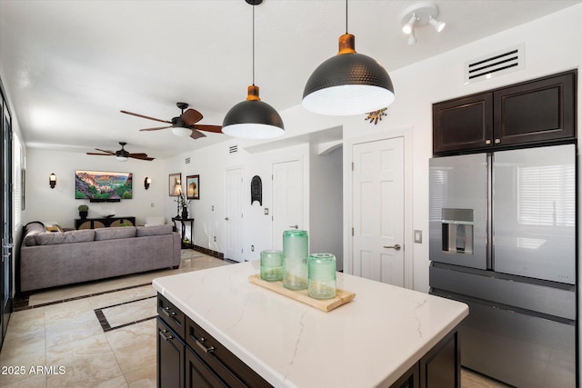 kitchen featuring dark brown cabinetry, visible vents, decorative light fixtures, a center island, and fridge with ice dispenser