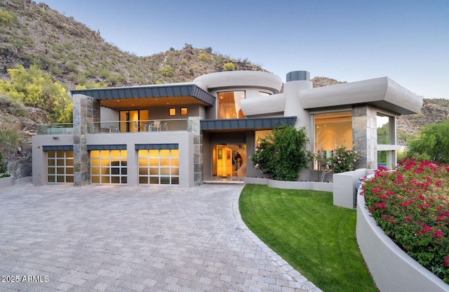 modern home featuring a balcony, a front lawn, decorative driveway, and stucco siding