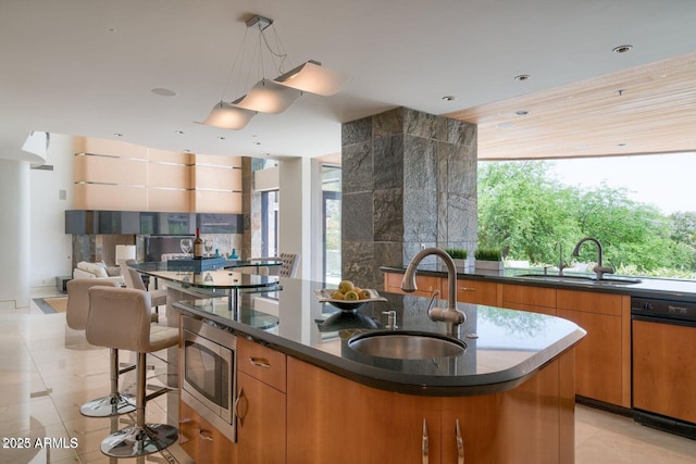 kitchen with stainless steel microwave, plenty of natural light, a sink, and a center island with sink