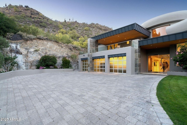 exterior space featuring stone siding, decorative driveway, a mountain view, and stucco siding