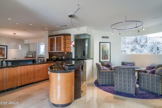 kitchen featuring brown cabinetry, dark countertops, open floor plan, and glass insert cabinets