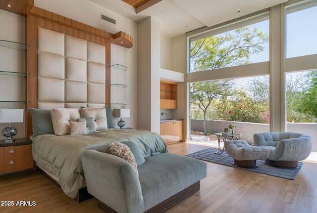 bedroom with expansive windows, a high ceiling, wood finished floors, and visible vents