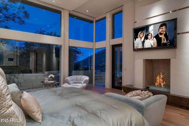 bedroom with a warm lit fireplace, a high ceiling, and wood finished floors