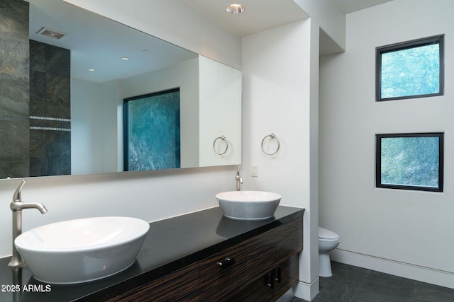 bathroom featuring toilet, double vanity, a sink, and visible vents