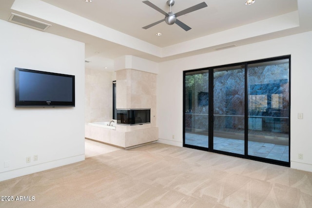 unfurnished living room featuring carpet floors, visible vents, a tray ceiling, and ceiling fan