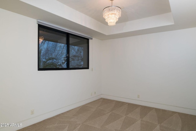 spare room with a chandelier, a raised ceiling, light colored carpet, and baseboards