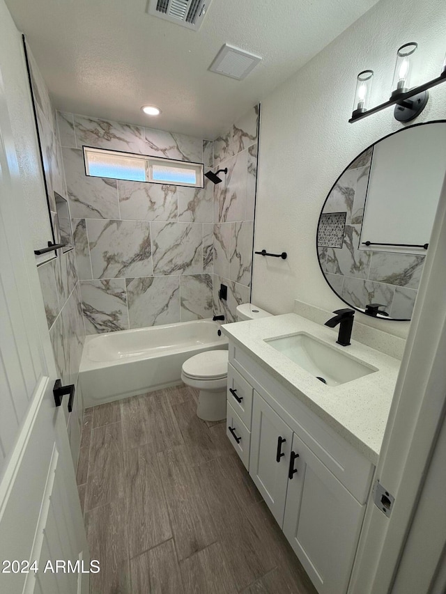 full bathroom featuring a textured ceiling, tiled shower / bath combo, vanity, and toilet